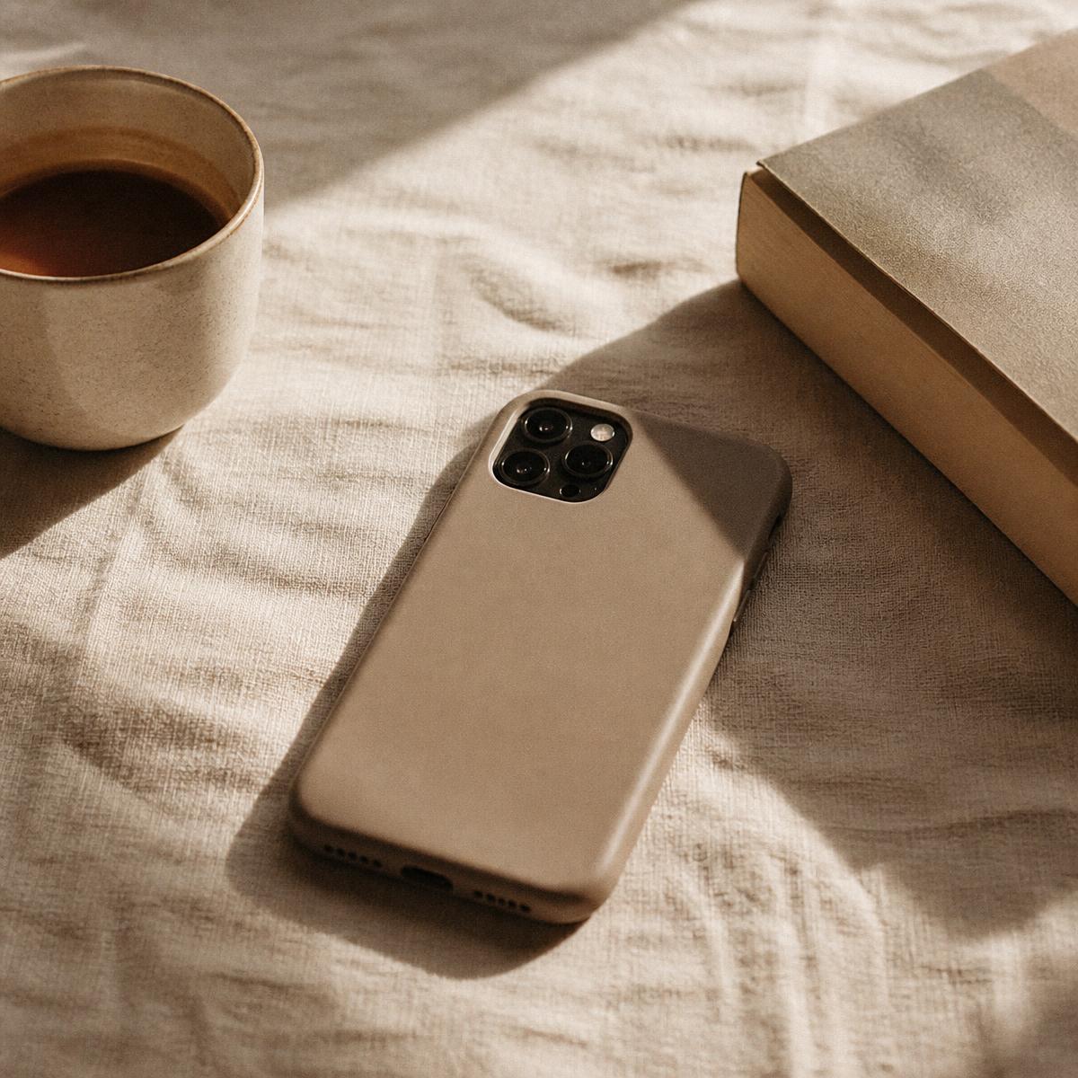 A phone face down beside a coffee cup and a book